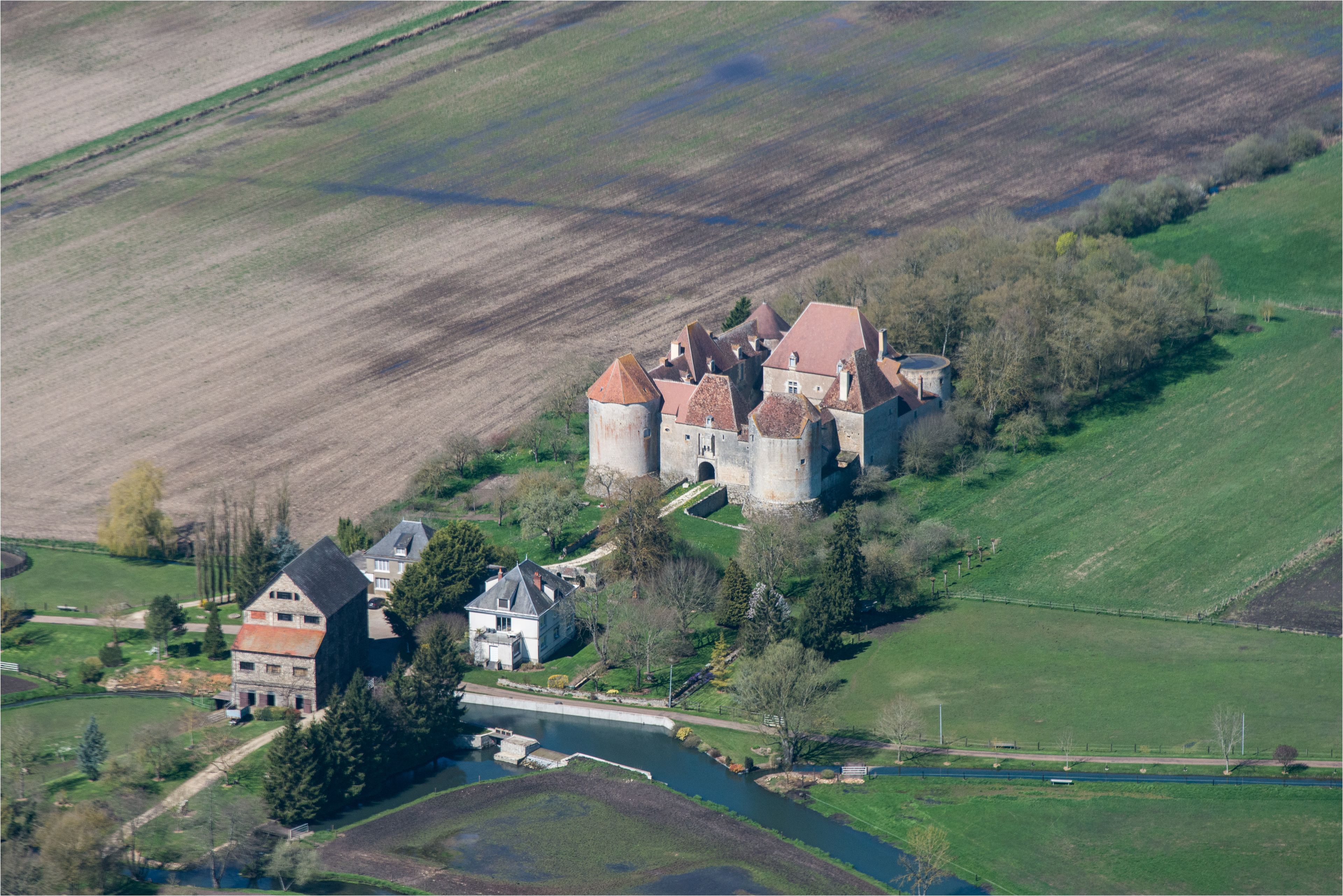 Un château doté de nombreuses tours, entouré de champs et bordé par une rivière.