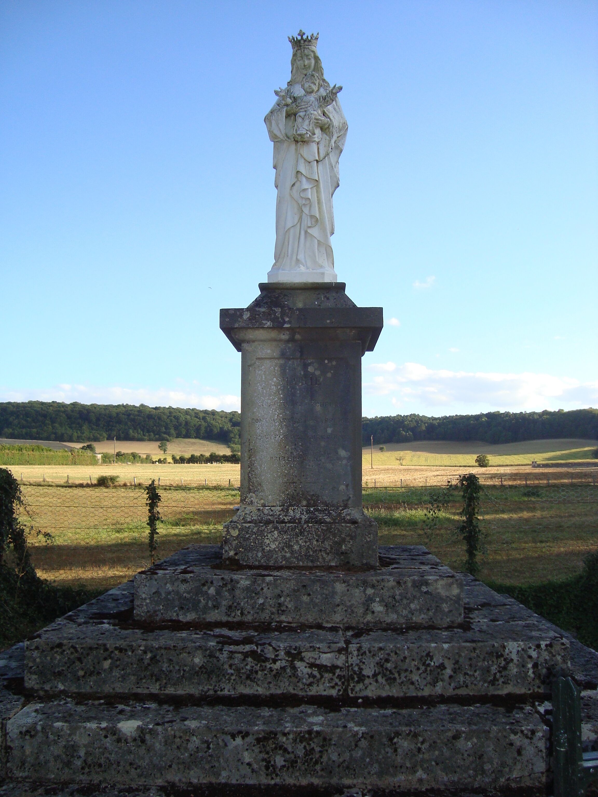 A statue on a pedestal with a rural landscape in the background.