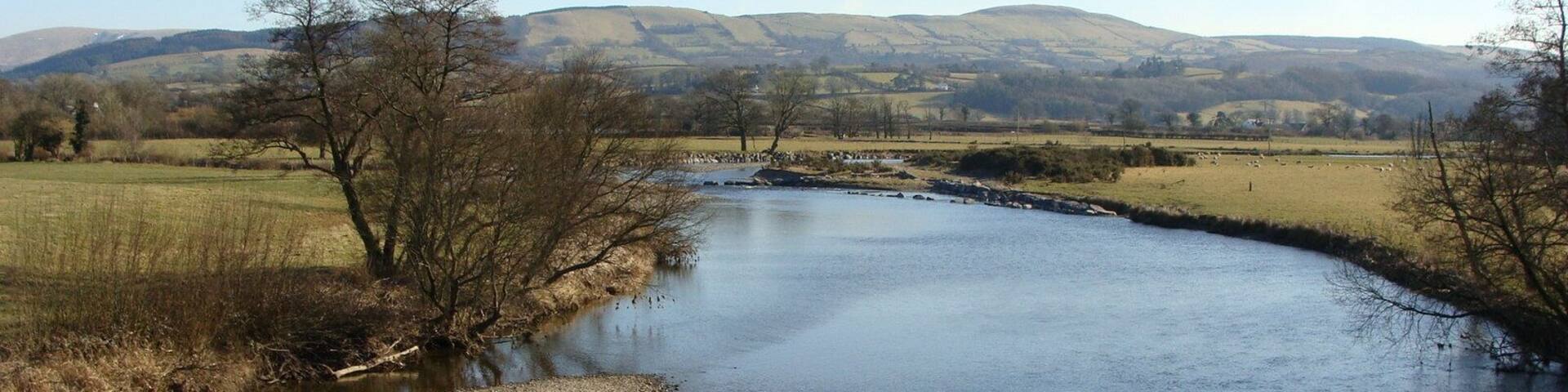 A river flowing through a rural landscape with hills in the background.