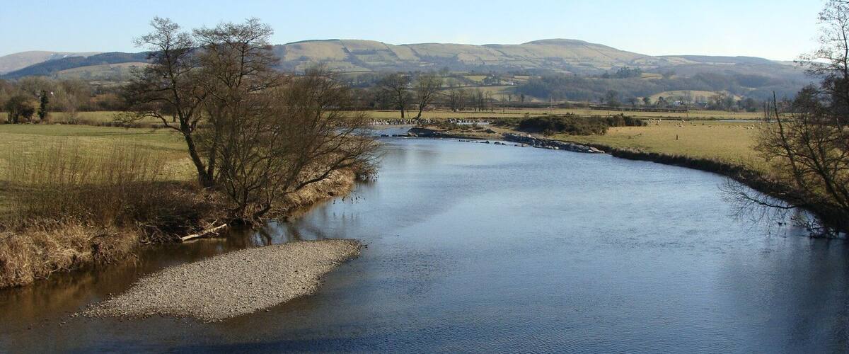 A river flowing through a rural landscape with hills in the background.