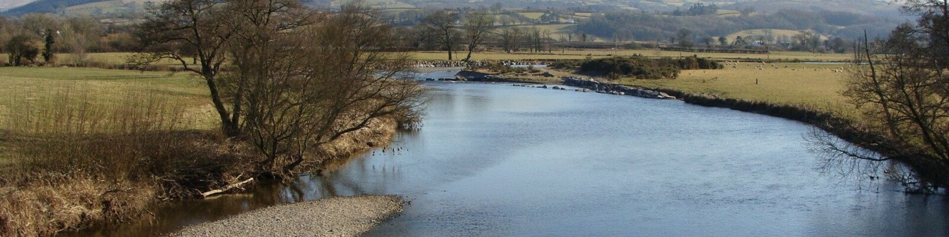 A river flowing through a rural landscape with hills in the background.