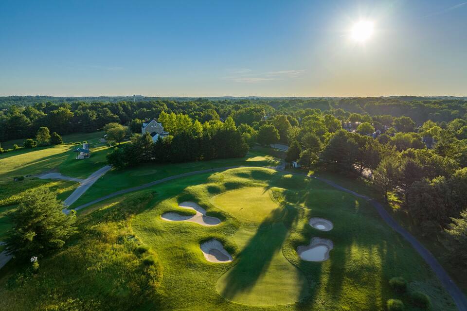 A golf course with bunkers and a clubhouse surrounded by trees.