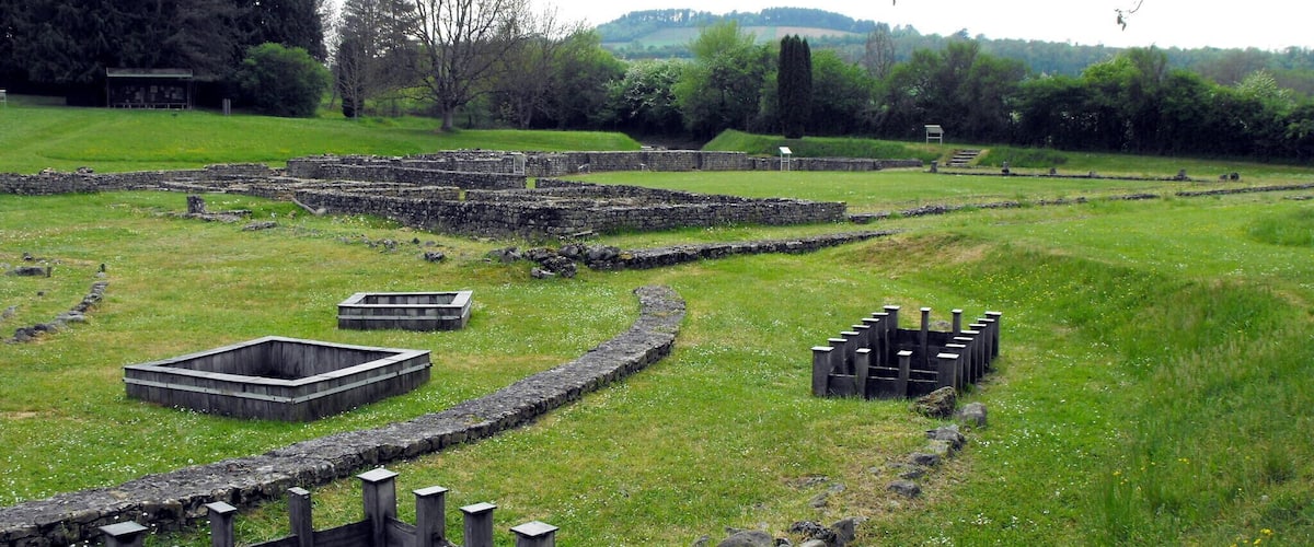 Ancient stone structures and ruins in a grassy field with trees and hills in the background.