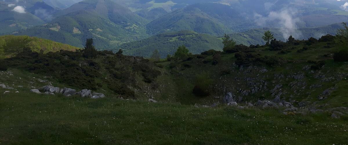 A mountainous landscape with green valleys and snow-capped peaks under a partly cloudy sky.