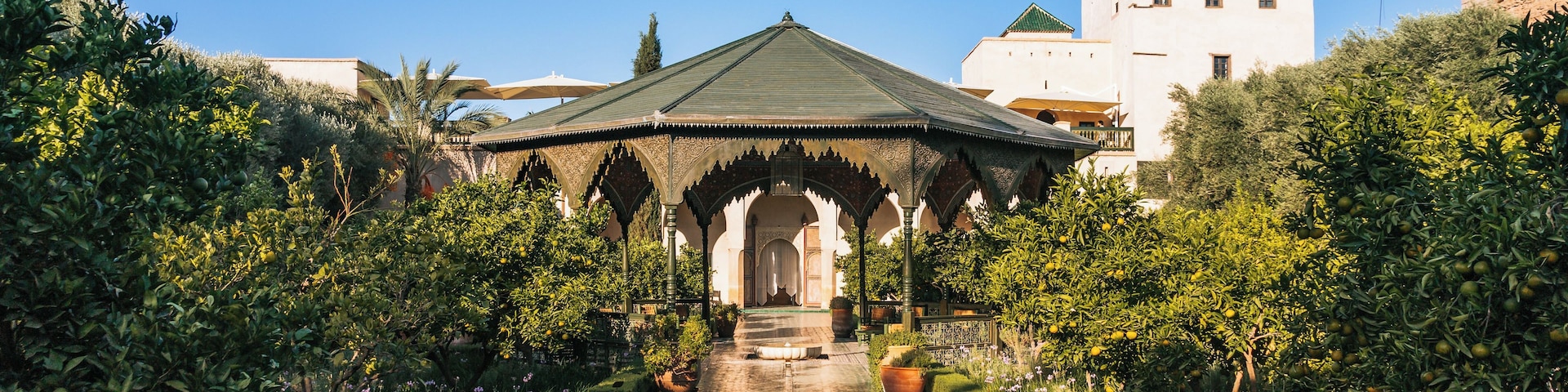 Un jardin avec une fontaine, un kiosque et un bâtiment en arrière-plan.