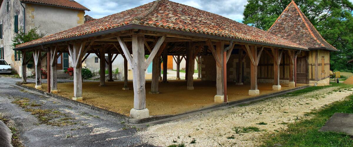 A traditional wooden pavilion with a tiled roof, surrounded by a gravel area and a building with a red-tiled roof.