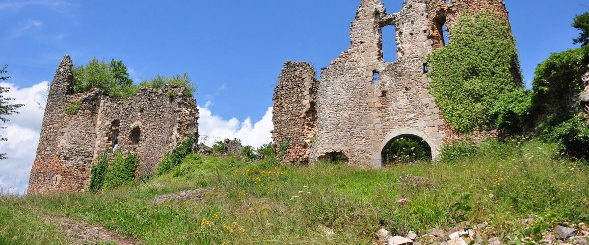 A ruined stone castle with arches and towers, surrounded by greenery and a clear blue sky.