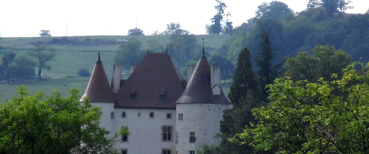 A castle with three towers, surrounded by greenery and hills.
