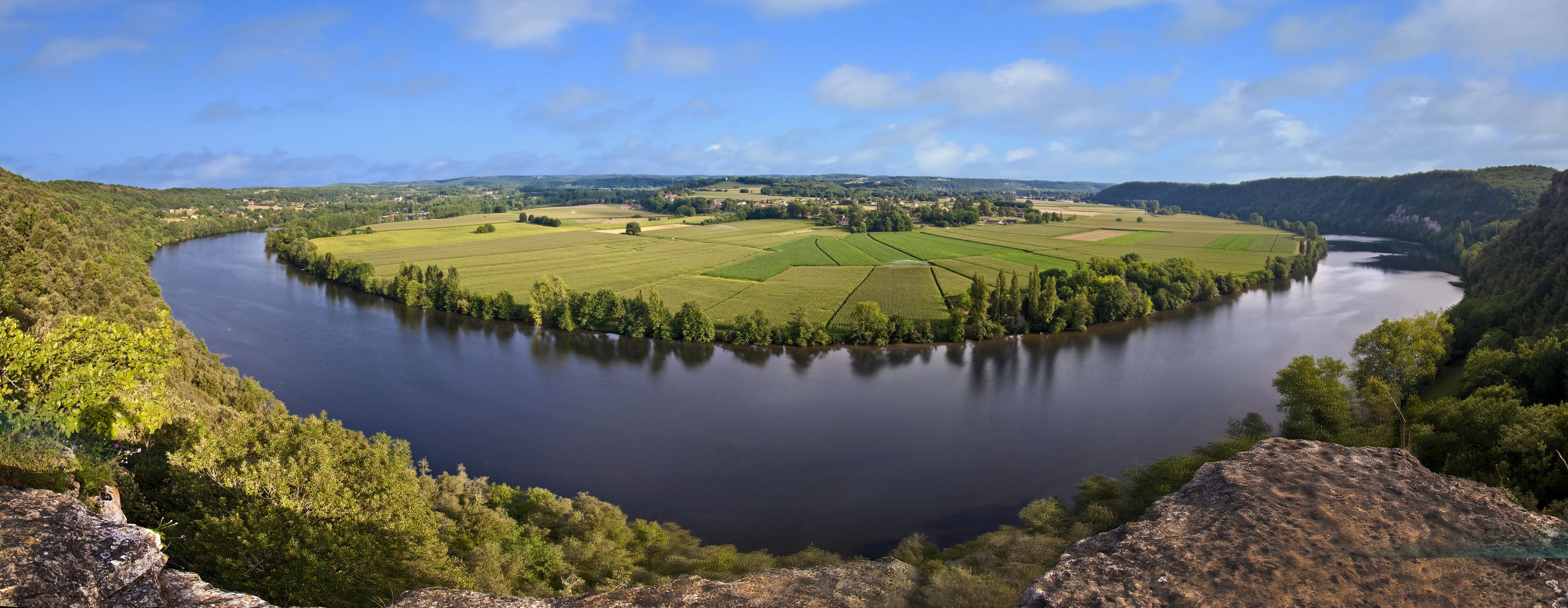 A river winding through a lush valley with green fields and forested hills.