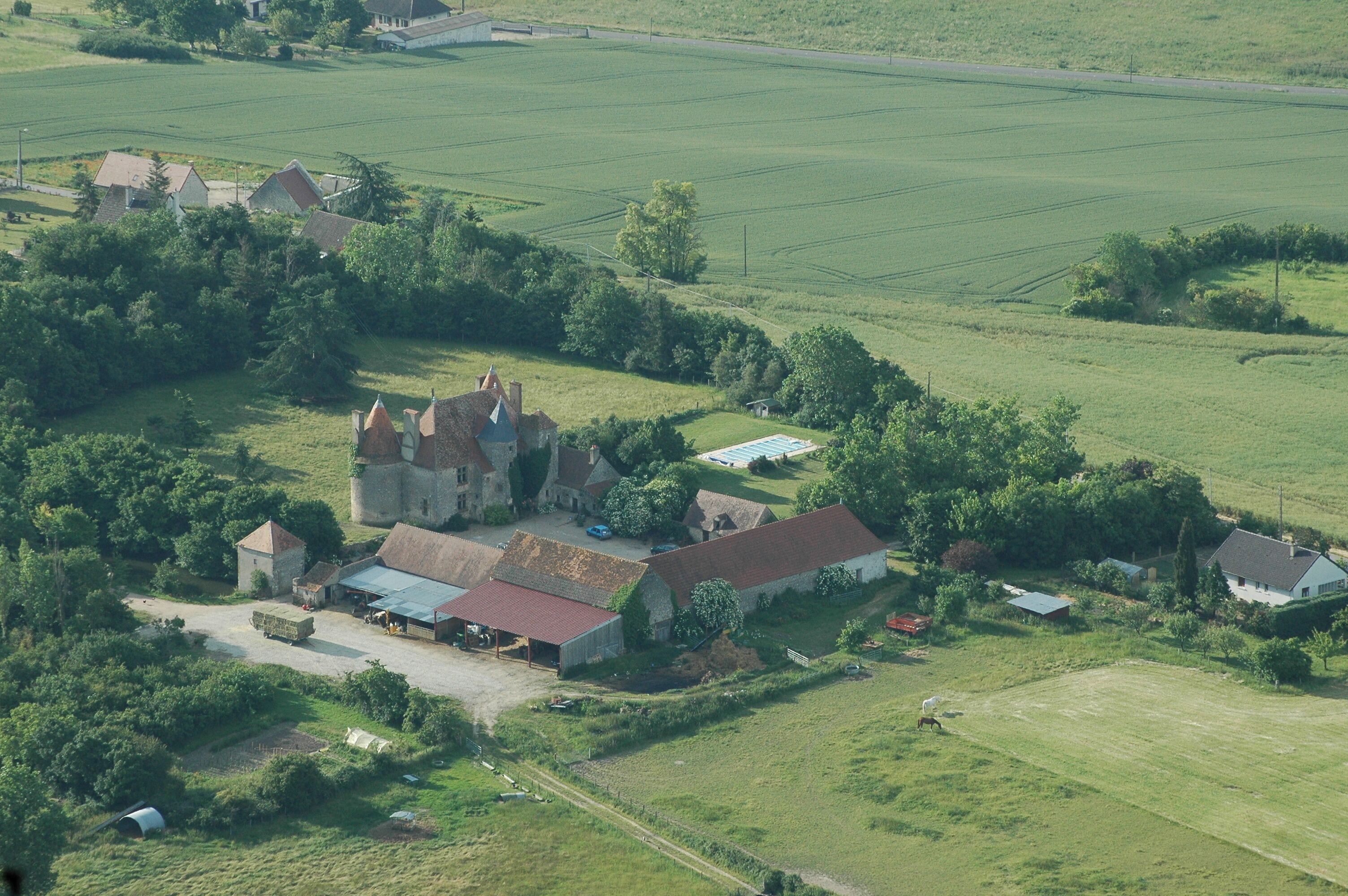 An aerial view of a rural area with a prominent castle-like structure surrounded by fields and smaller buildings.