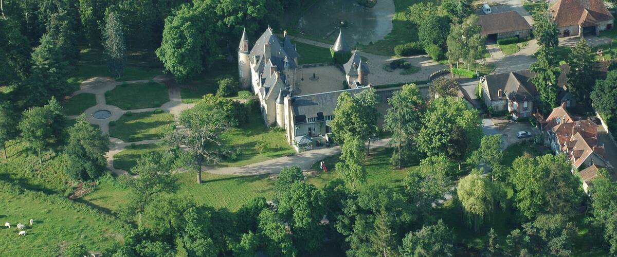 An aerial view of a castle surrounded by lush greenery and a river.