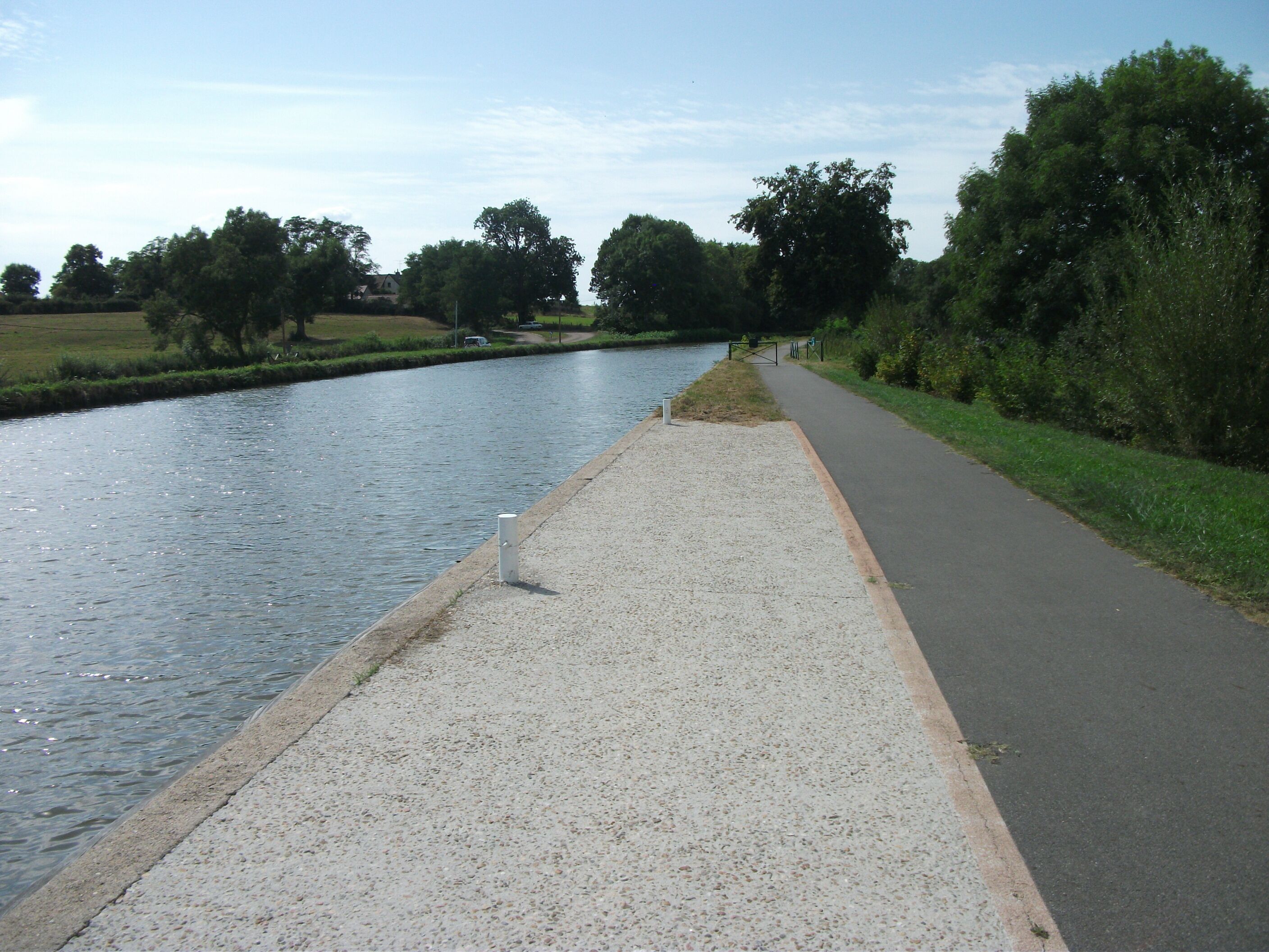 A river with a paved walkway alongside it, bordered by trees and greenery.
