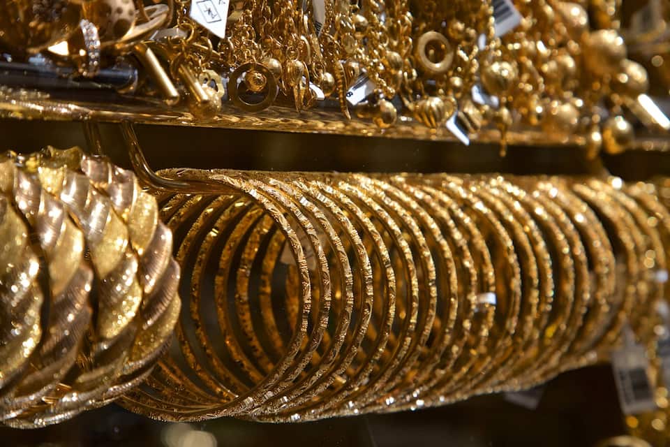 En samling av detaljrikt utformade guldsmycken, inklusive armband och ringar, som visas upp i en butik.