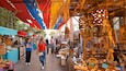 A bustling outdoor market with colorful stalls and wooden sculptures.
