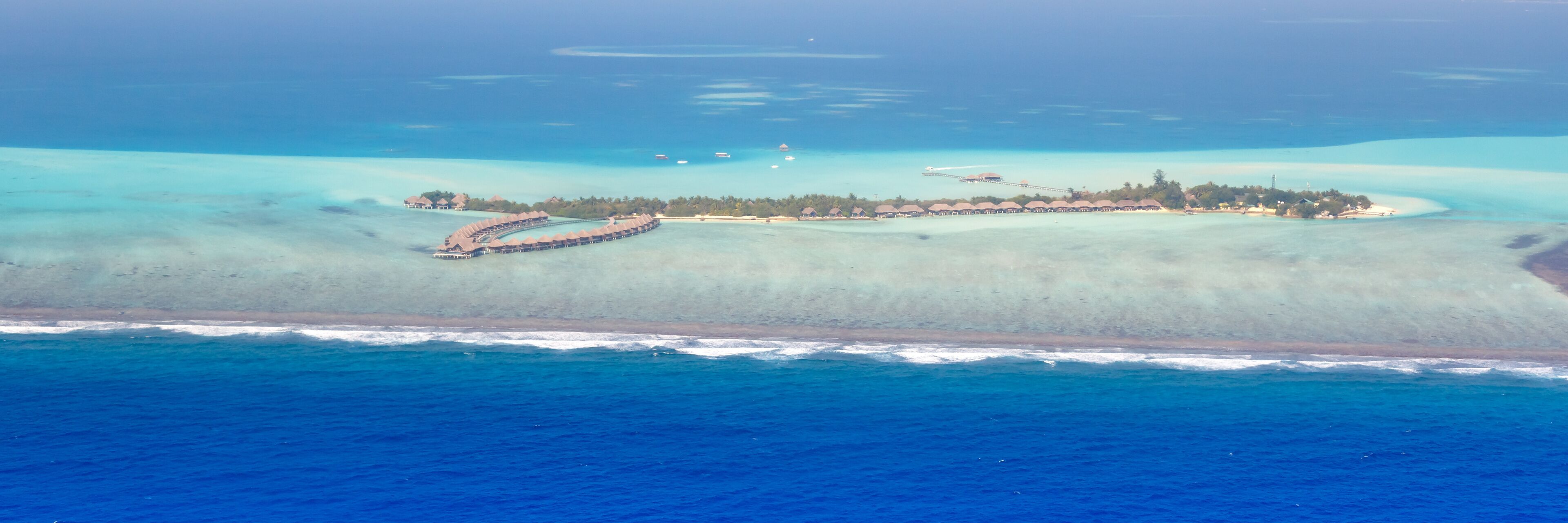 An aerial view of a resort island with overwater bungalows and a pier.