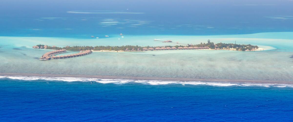 An aerial view of a resort island with overwater bungalows and a pier.