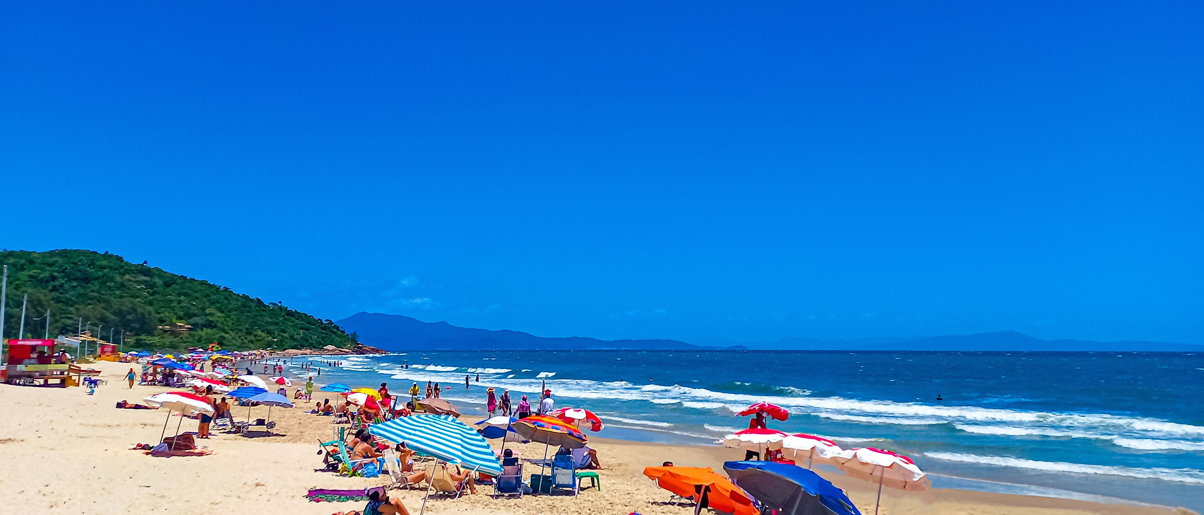 A crowded beach with colorful umbrellas and people relaxing on the sand.