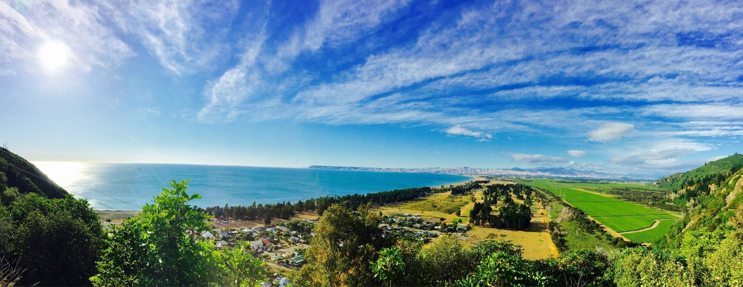 A coastal landscape with a clear sky, green fields, and a distant view of the sea.