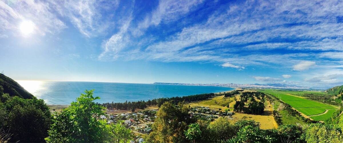 A coastal landscape with a clear sky, green fields, and a distant view of the sea.