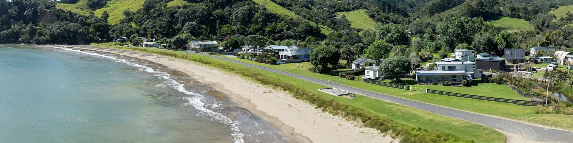 A coastal landscape with a sandy beach, a road, and houses on a hillside.