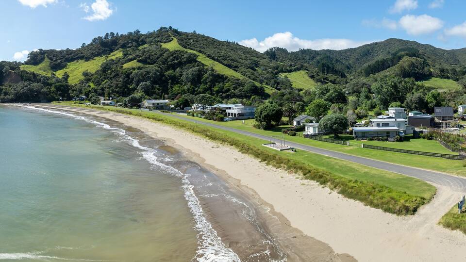 A coastal landscape with a sandy beach, a road, and houses on a hillside.