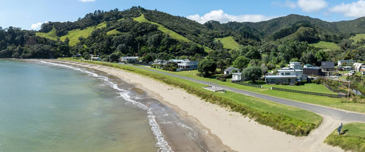 A coastal landscape with a sandy beach, a road, and houses on a hillside.
