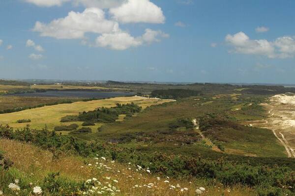 A coastal landscape with a sandy beach, turquoise waters, and rolling hills.