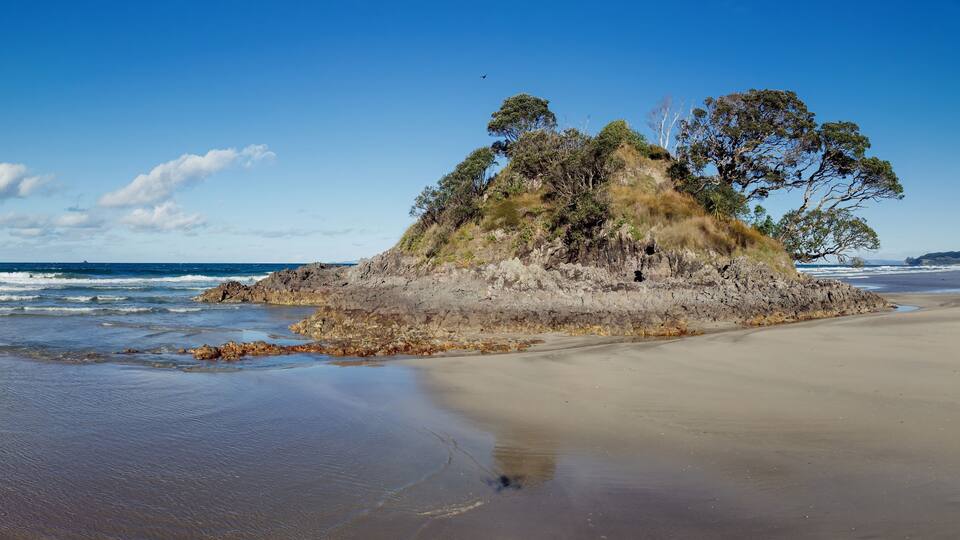 A sandy beach with a rocky outcrop covered in trees.
