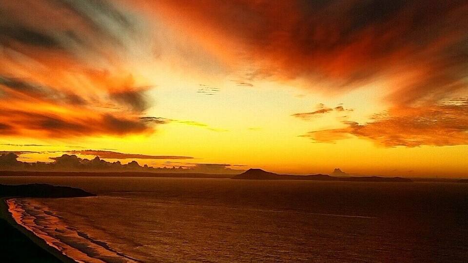 A sunset over a beach with waves and distant mountains.
