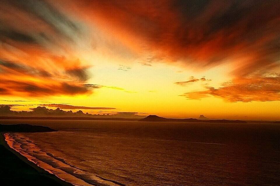 A sunset over a beach with waves and distant mountains.
