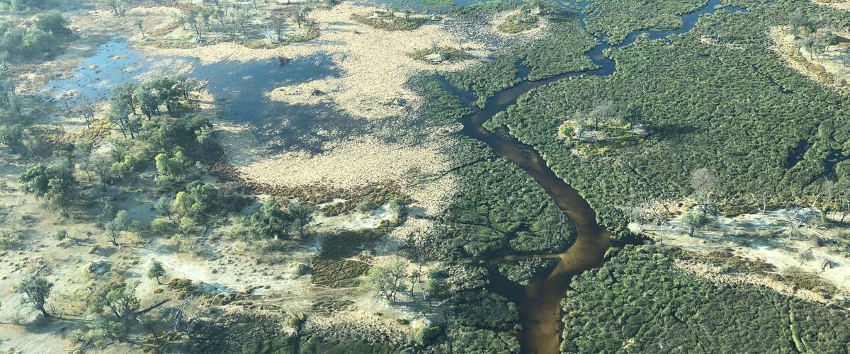 An aerial view of a river winding through a landscape with patches of greenery and dry, sandy areas.