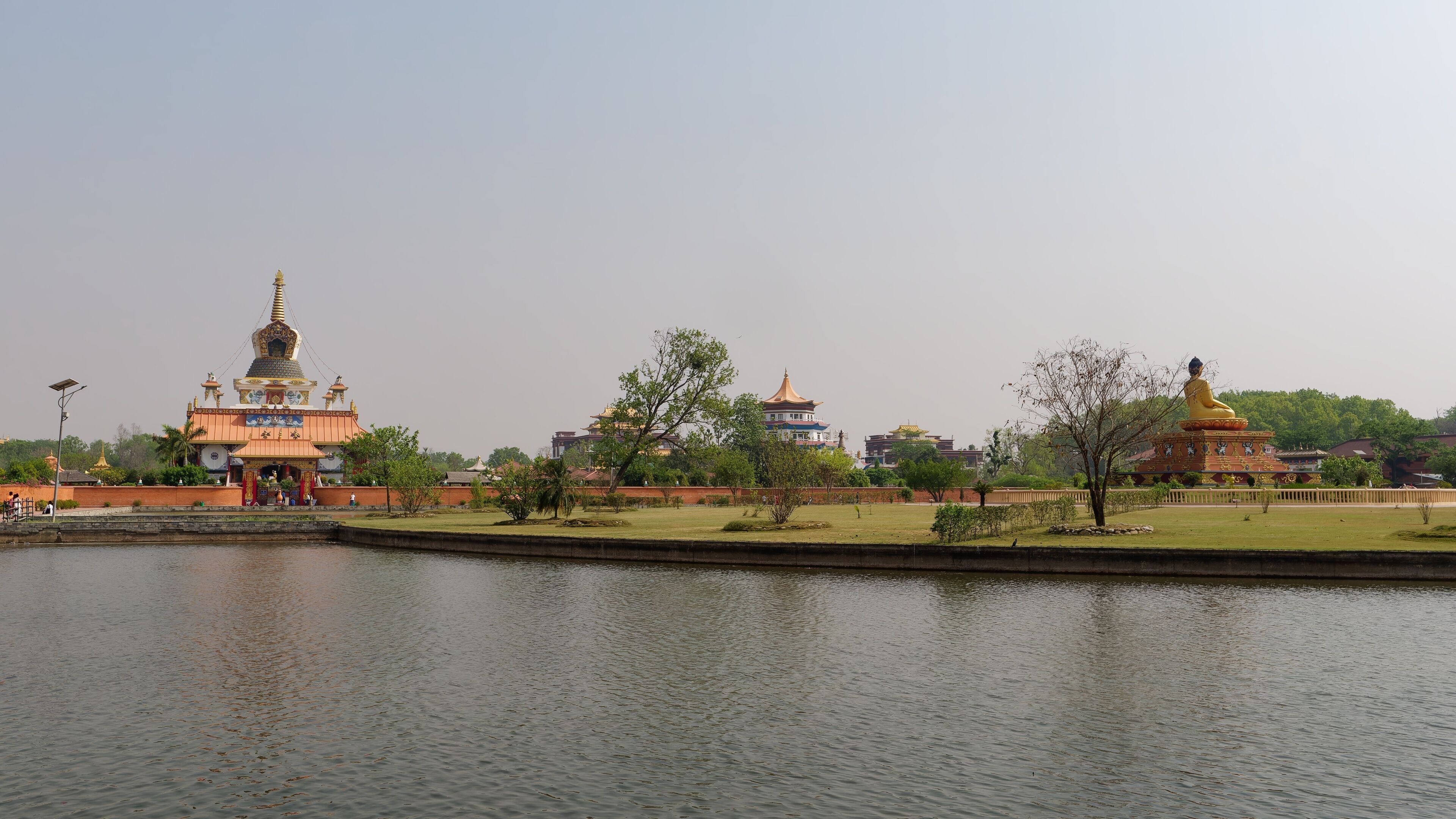 Serene view of a Buddhist temple and statue by a pond in Lumbini, Nepal under a clear sky