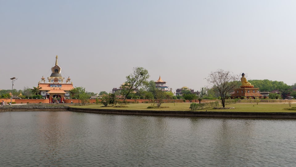 A serene lakeside view with traditional architecture, including pagodas and a large Buddha statue.