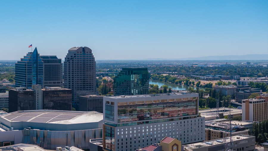 Aerial perspective of Sacramento, California, highlighting the Golden 1 Center, high rise buildings, and the Sacramento River under a clear blue sky.