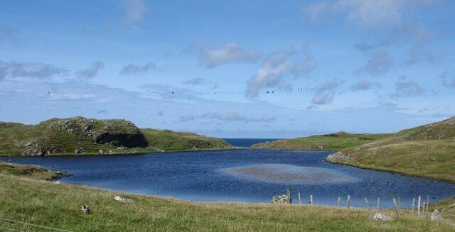 A lake surrounded by grassy hills and a clear sky.