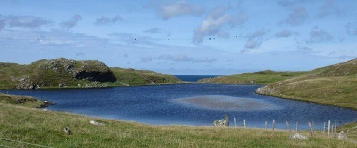 A lake surrounded by grassy hills and a clear sky.
