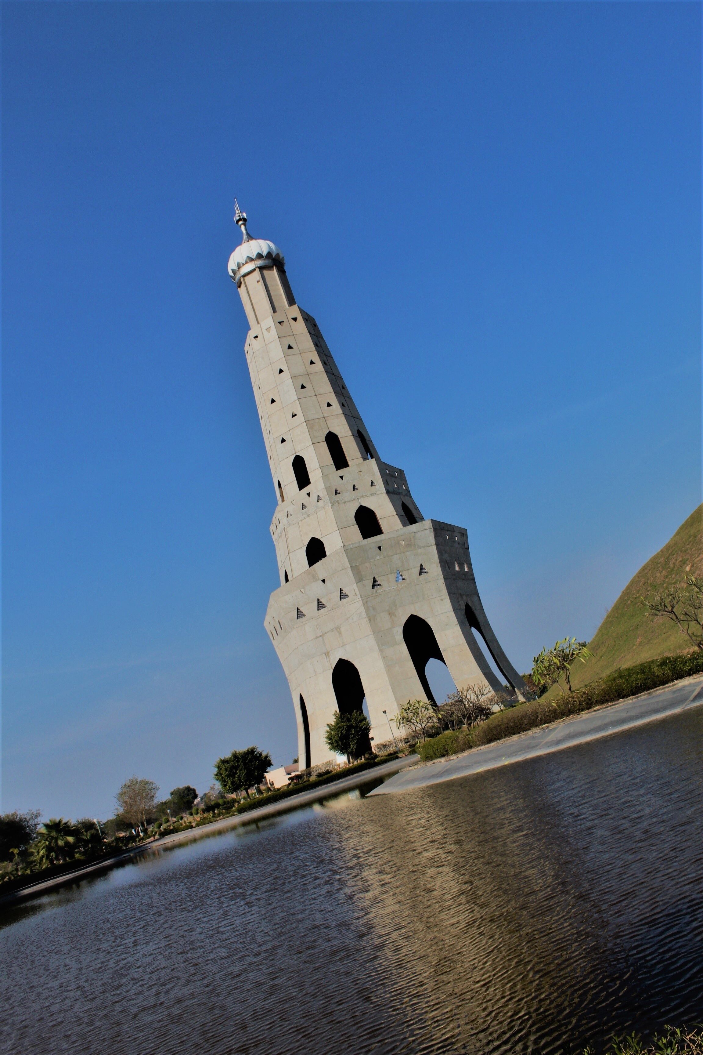 A beautiful huge tower just near a small pond standing tall in clear sky in chandigarh, india.