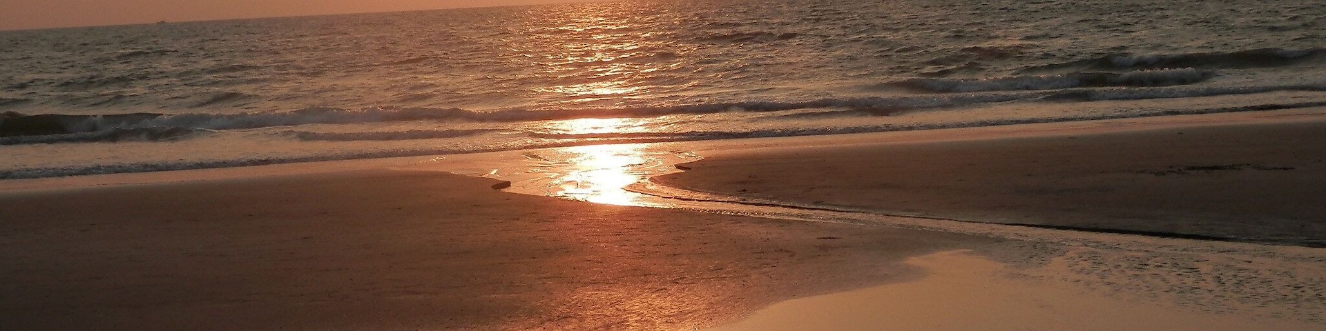 Una playa al atardecer, con el sol reflejándose en la arena húmeda y el agua.