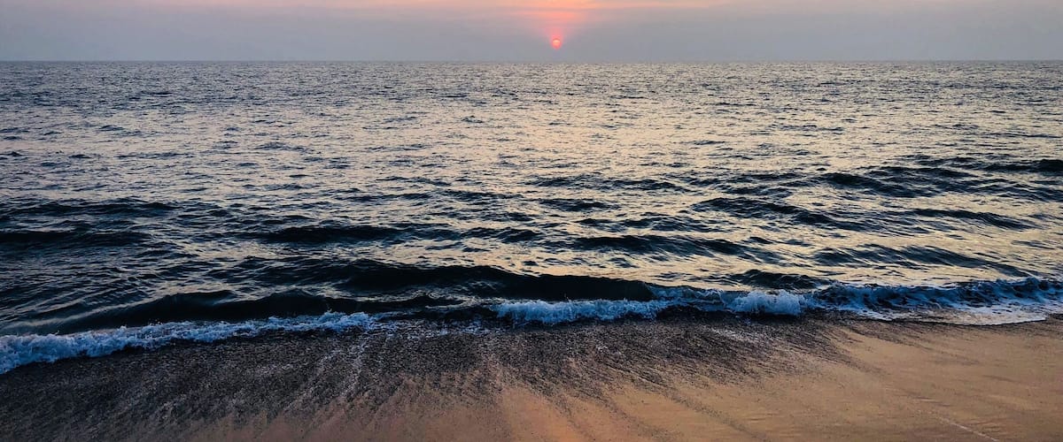 A beach with waves and a sunset in the distance.