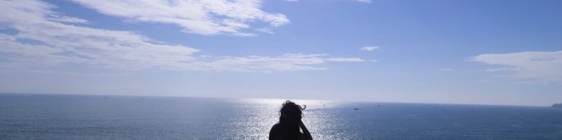 Una persona sentada sobre un risco con vista al océano, bajo un cielo despejado.