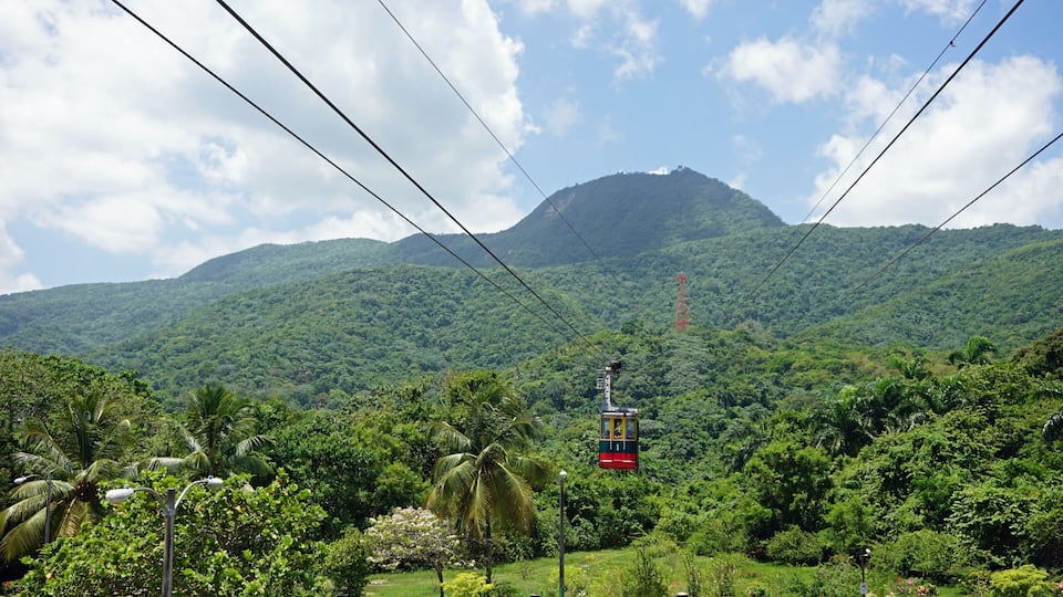 A cable car in a lush green valley with a mountain in the background.