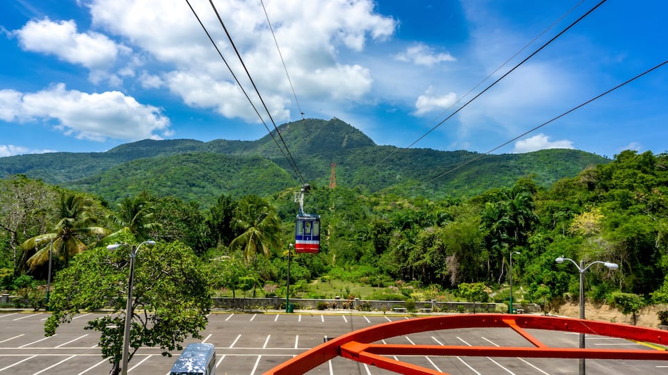 A cable car on a mountain with lush greenery and a clear sky.