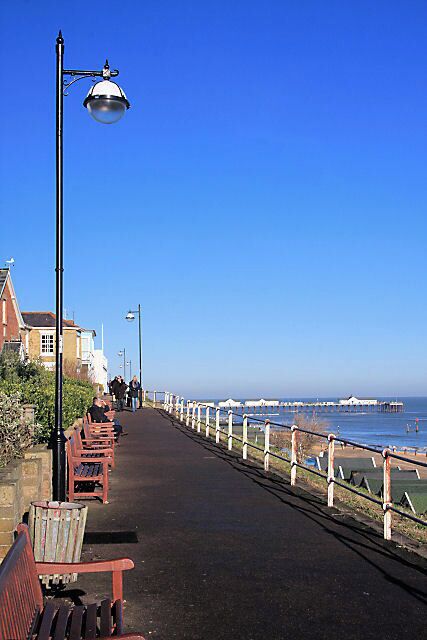 A seaside promenade with benches, a white railing, and a clear blue sky.