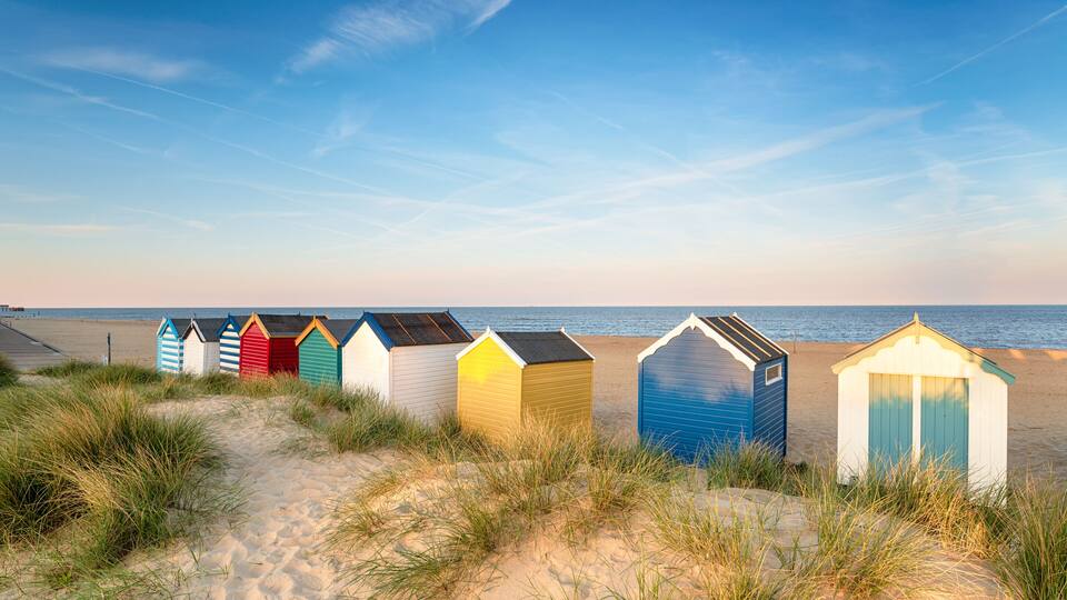 A sandy beach with colorful beach huts and the ocean in the background.