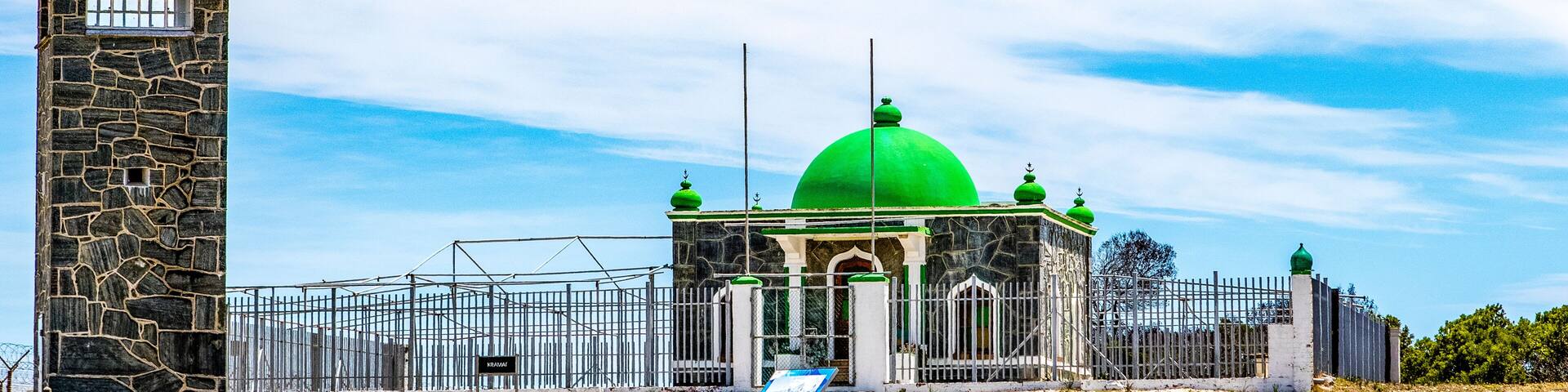 Una torre de piedra, un edificio con cúpula verde y una valla metálica.