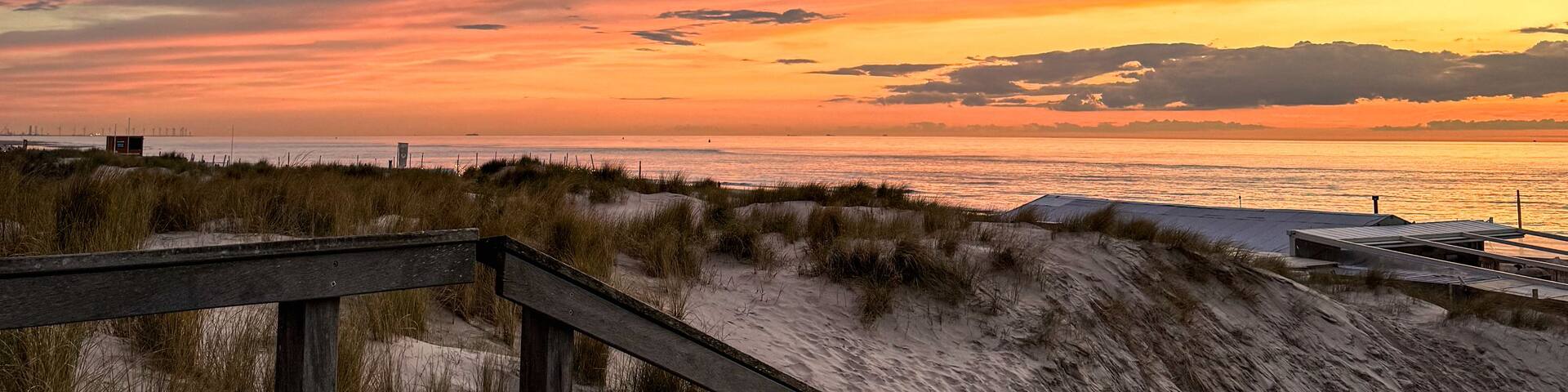 A sunset over a beach with a wooden boardwalk and dunes.