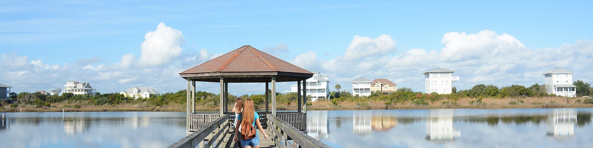 Girl with backpack hiking on her vacation. Friends walking on the pier, houses in the background, North Topsail Beach, North Carolina.; Shutterstock ID 430564006