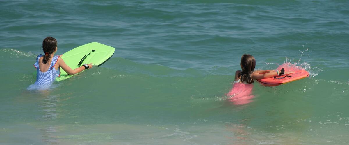 Two individuals in the water, each holding a surfboard.