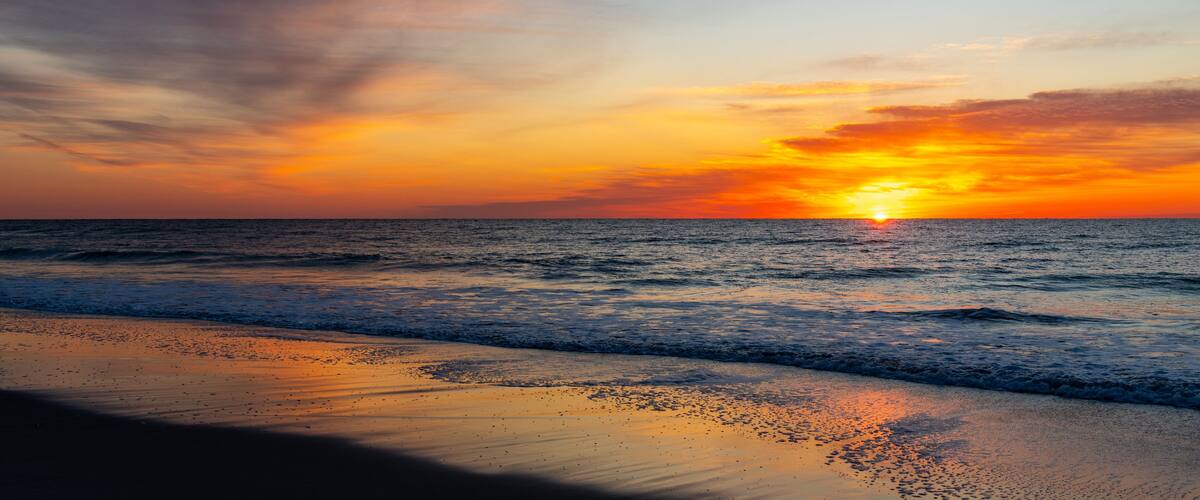 A sunset over the ocean with a beach in the foreground.