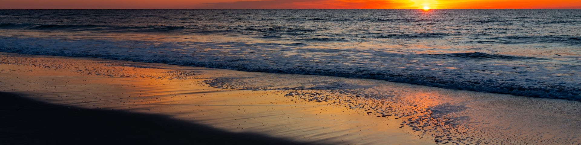 A sunset over the ocean with a beach in the foreground.